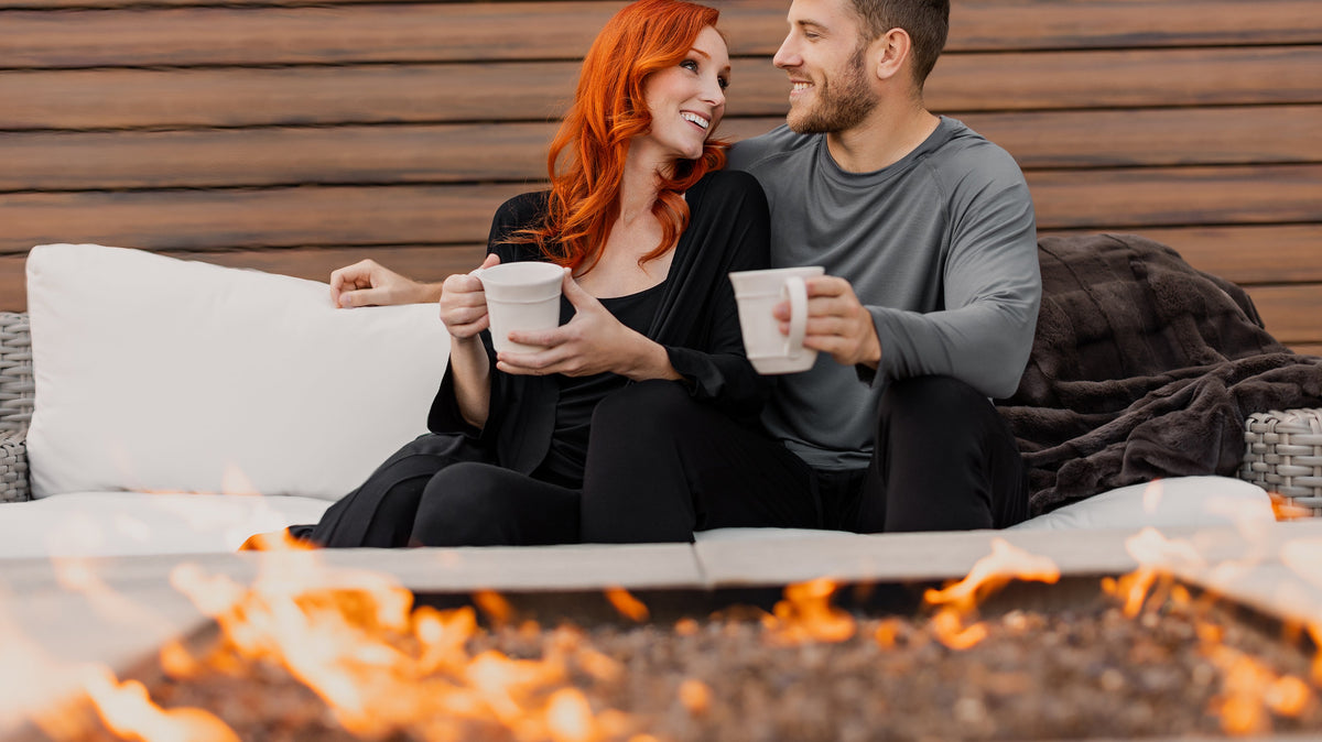 Couple sitting together outside by the fire wearing organic, bamboo pajamas from Earthly Threads