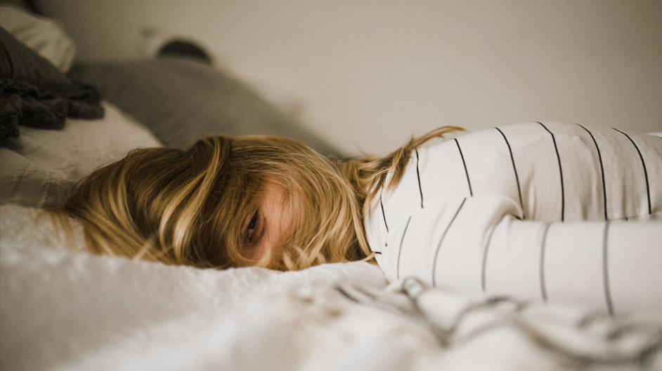 Kid trying to sleep in bed looking tired but has one eye open