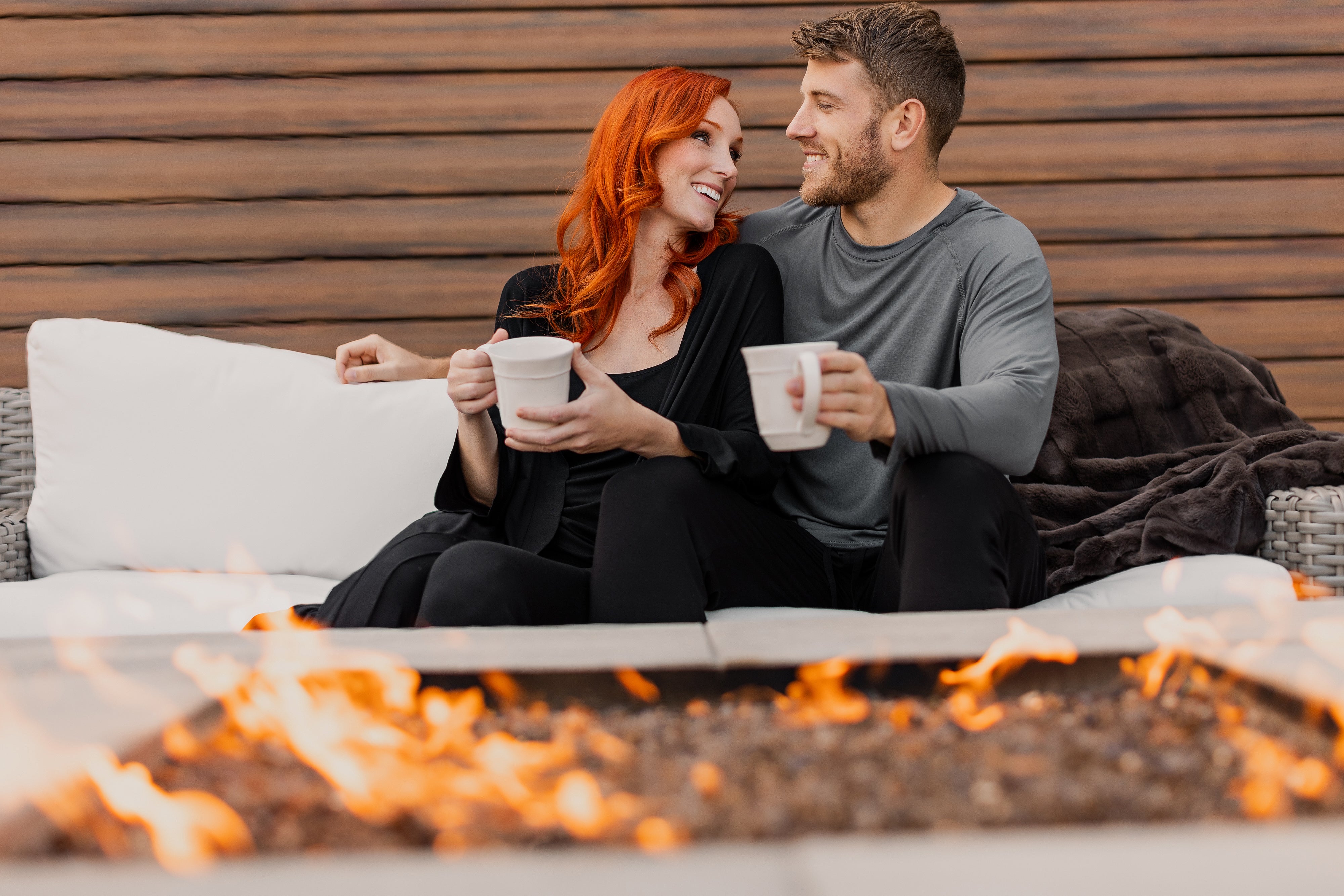 Couple sitting together outside by the fire wearing organic, bamboo pajamas from Earthly Threads