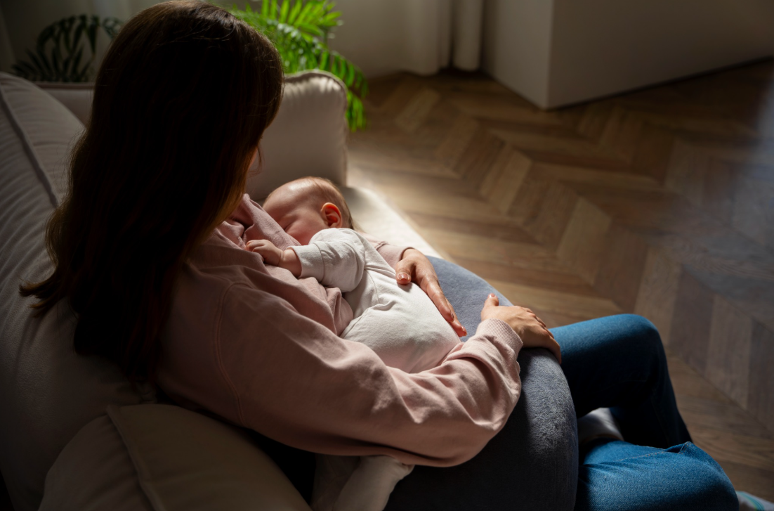 A mother cradles her sleeping newborn while sitting in a softly lit living room.