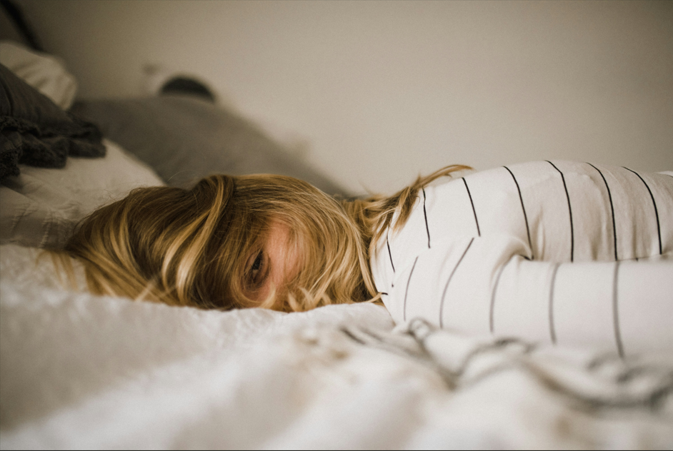 Kid trying to sleep in bed looking tired but has one eye open